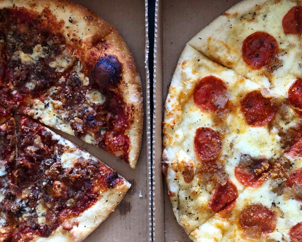 Two full pan pizzas are side by side. One has dark sauce and no cheese, and the other is pepperoni with lots of cheese. Photo by Alyssa Buckley.