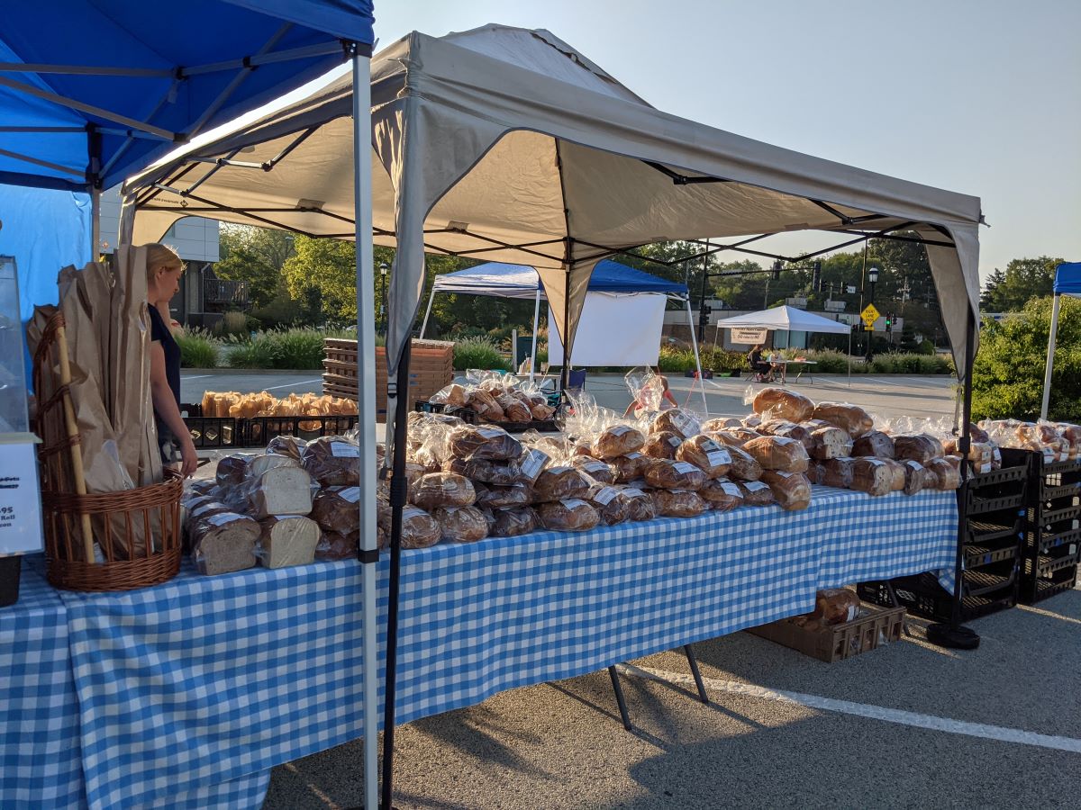 Various breads sitting atop tables with blue and white checkered tablecloths. The tables are underneath blue and beige tents. Photo by Tias Paul.