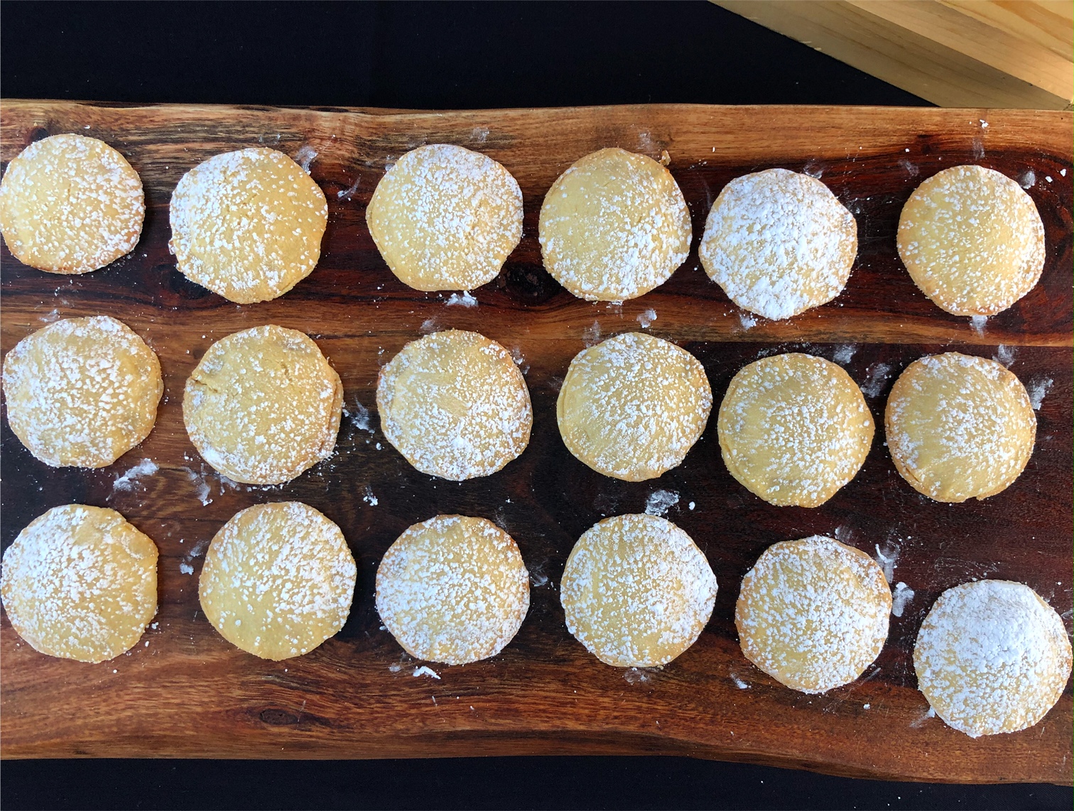 On a dark wooden board, there are lemon cookies dusted with powdered sugar. Photo by Alyssa Buckley.