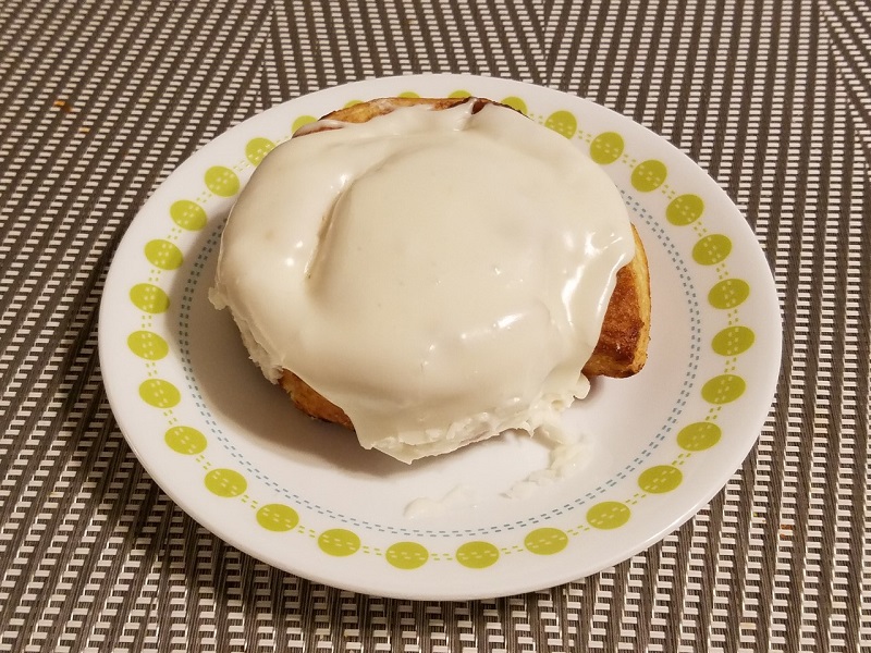 A flaky cinnamon roll on a small plate with frosting covering the entire roll and about half of the sides of the roll. Photo by Matthew Macomber.