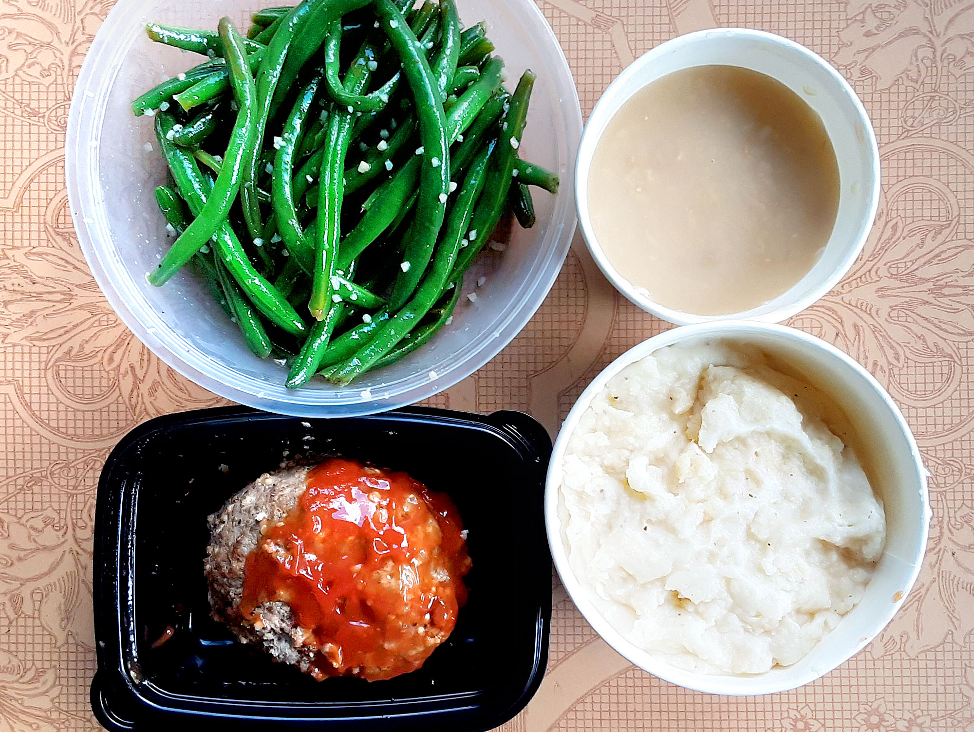 On a pink tablecloth, there are four dishes with dinner: green beans, gravy, mashed potatoes, and a circle meatloaf. Photo by Paul Young.