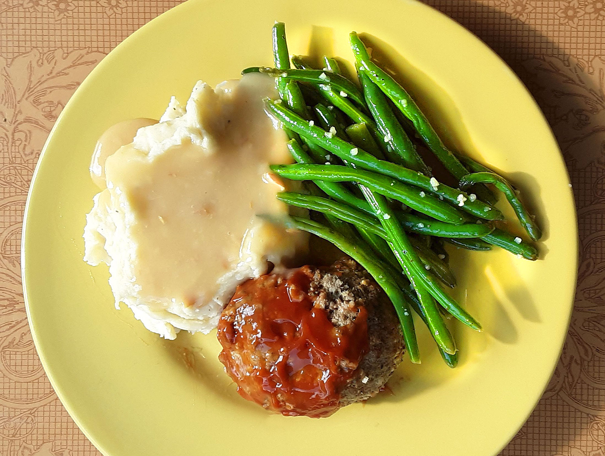 On a round, yellow plate, the author's dinner is a scoop of mashed potatoes with light gravy, many green beans topped with garlic, and a circle meatloaf. Photo by Paul Young.