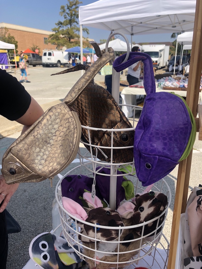 Small chameleon-shaped pouches (gold, golden brown, and purple) hang by their tails from a white display rack at Fabrikateâ€™s booth at Urbanaâ€™s Market at the Square. On the rack below, bunny pouches. Photo by Dani Nutting.