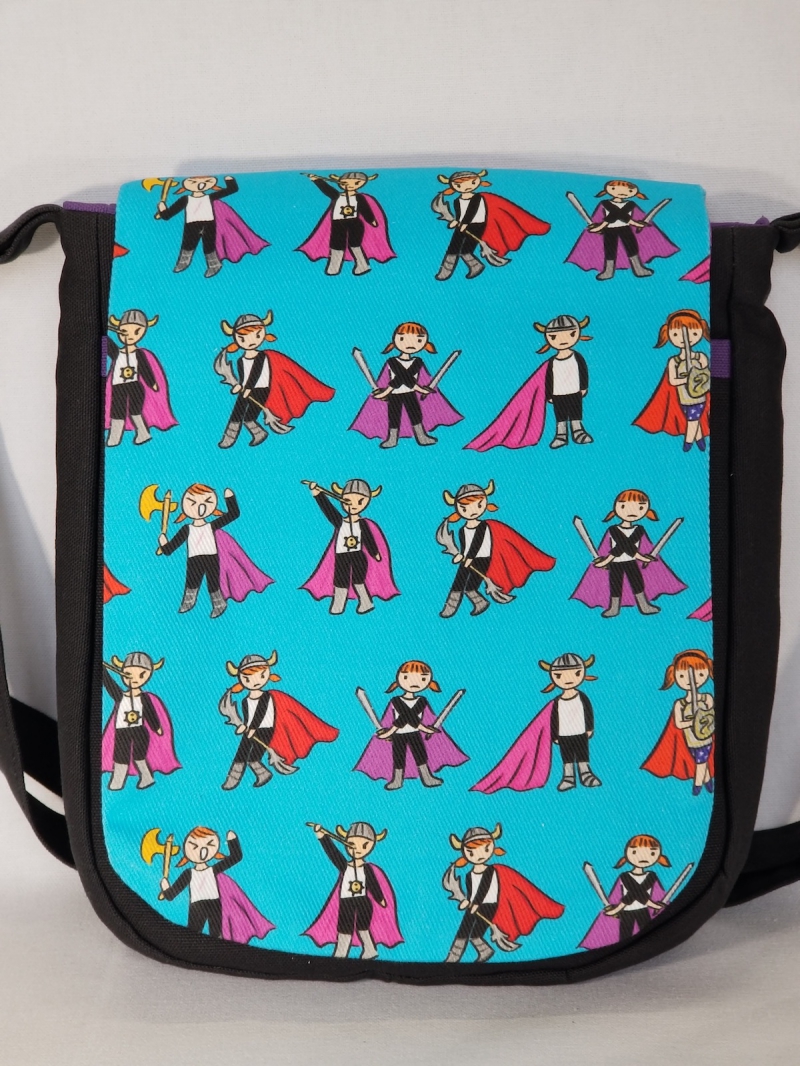 Kobakâ€™s â€œWee Vikingâ€ bag against a plain white background. Fabric is bright turquoise with small, red-haired Vikings standing in various poses. Some have a helmet & weapons; all are wearing a pink or red cape. Photo by Kate Kobak.