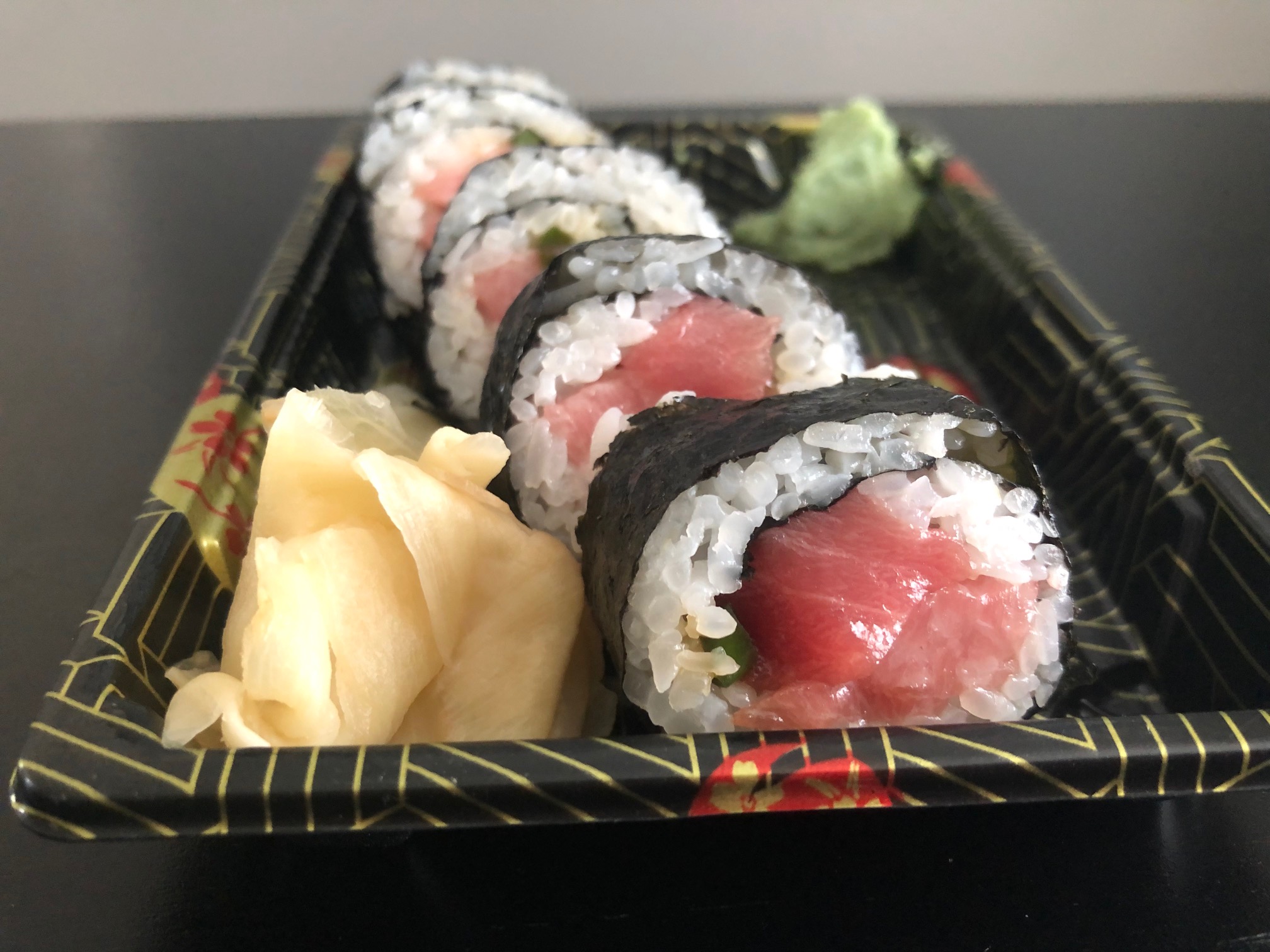 From the side, a tuna sushi roll sits in a rectangular takeout container with pickled ginger beside it. Photo by Alyssa Buckley.