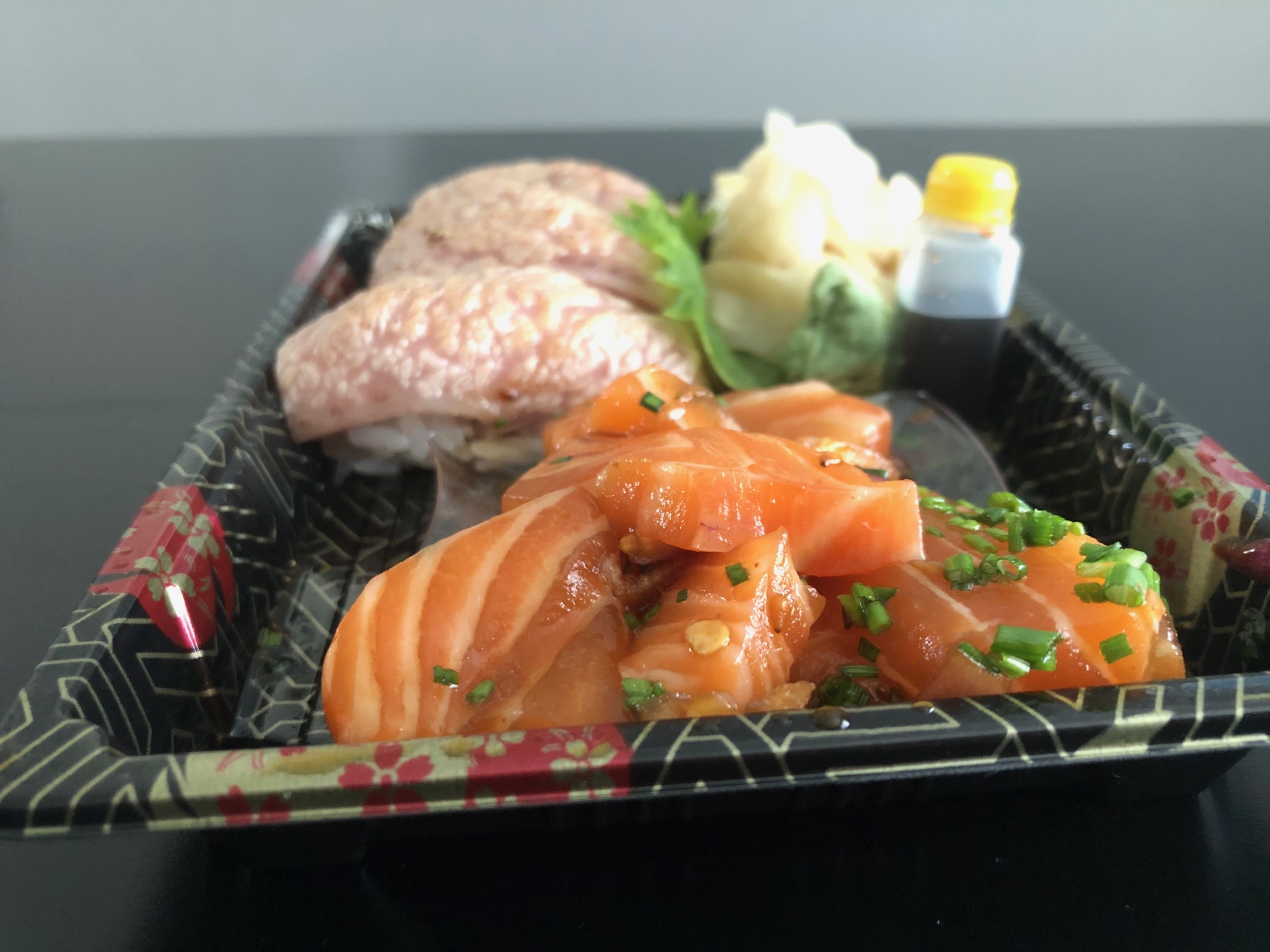 From the side, the rectangular takeout tray shows marinated raw salmon chunks with specks of green onion. Behind the salmon poke, is seared tuna. Photo by Alyssa Buckley.