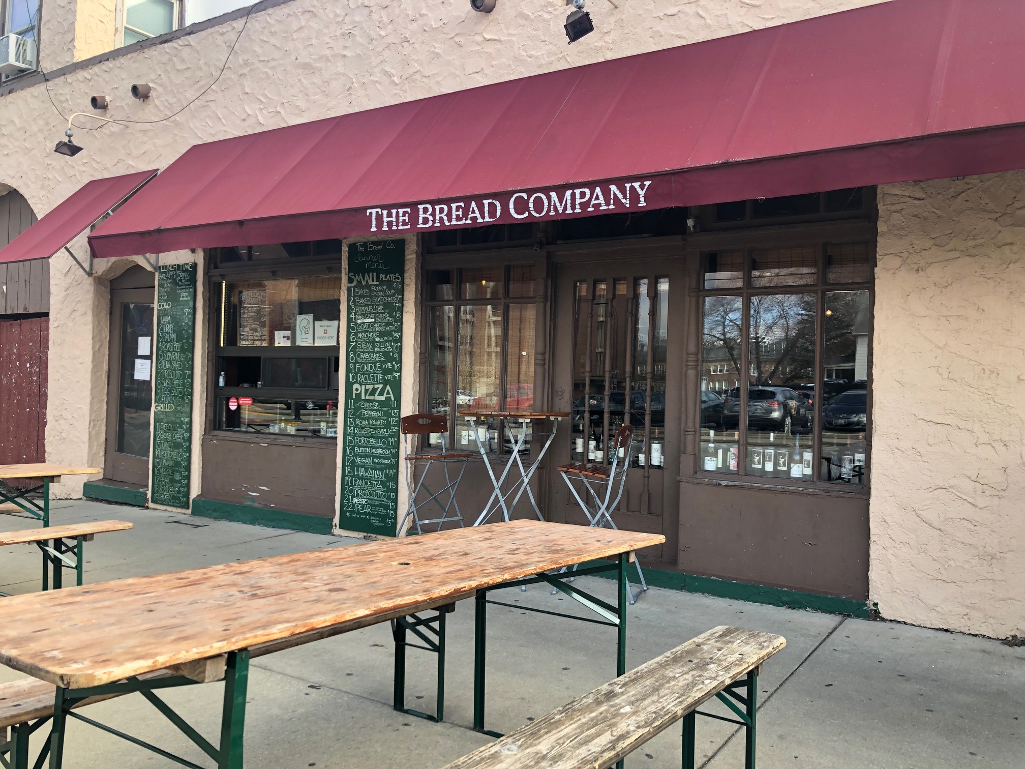 The exterior of The Bread Company has a burgundy awning with the restaurant's name on the light brown stucco outside with long wooden tables out front. Photo by Alyssa Buckley.