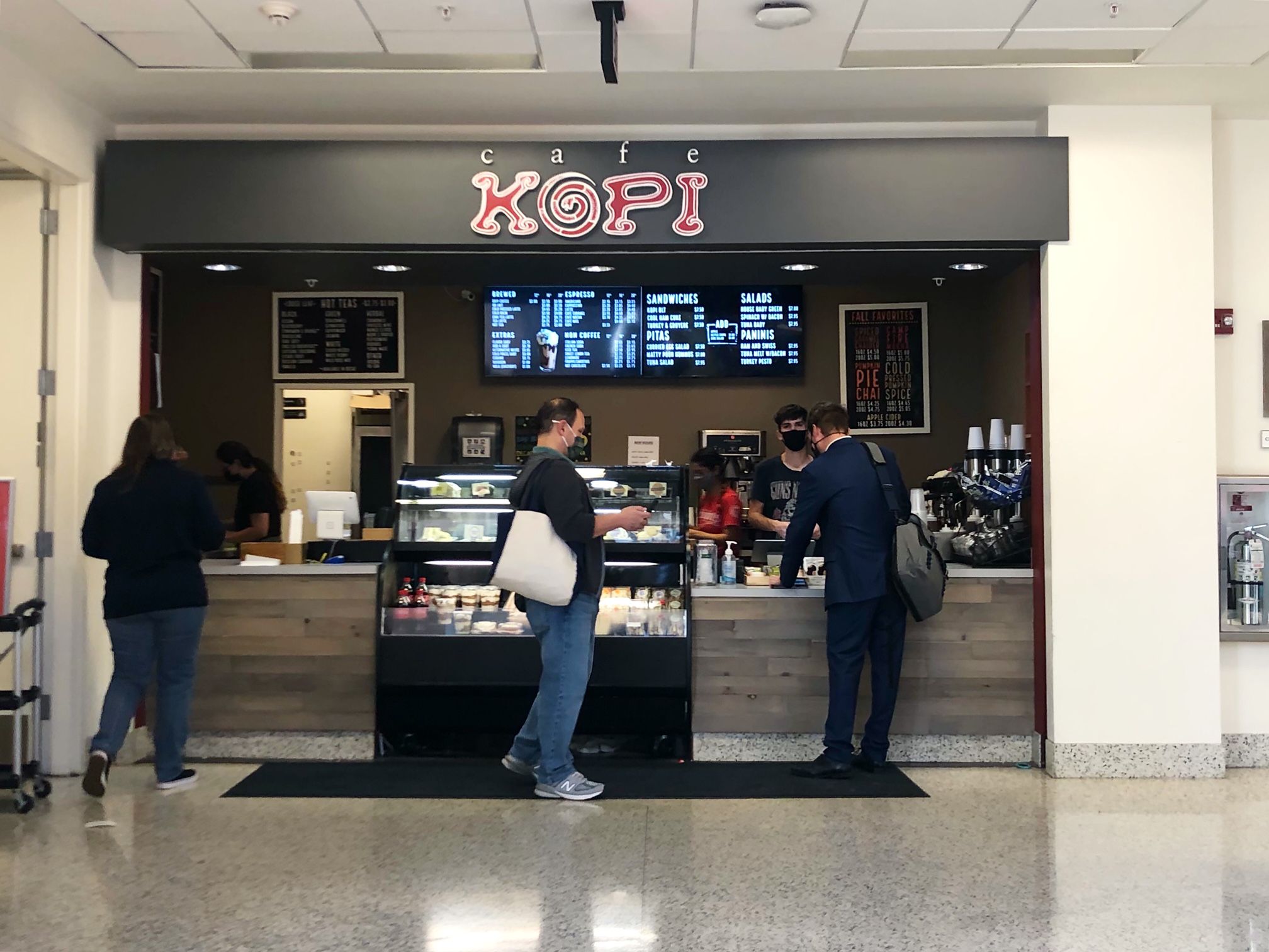 The campus location of Cafe Kopi has a black restaurant sign above where three white partons are ordering coffee and lunch inside the BIF at U of I. Photo by Alyssa Buckley.