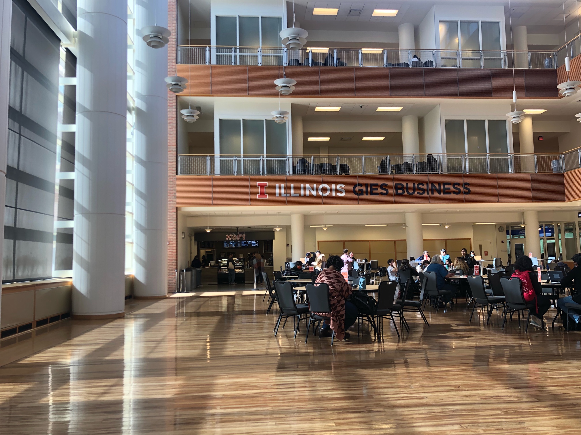 An interior photo of the U of I's Geis College of Business shows the large open foyer with wooden flooring and tables filled with students. Photo by Alyssa Buckley.