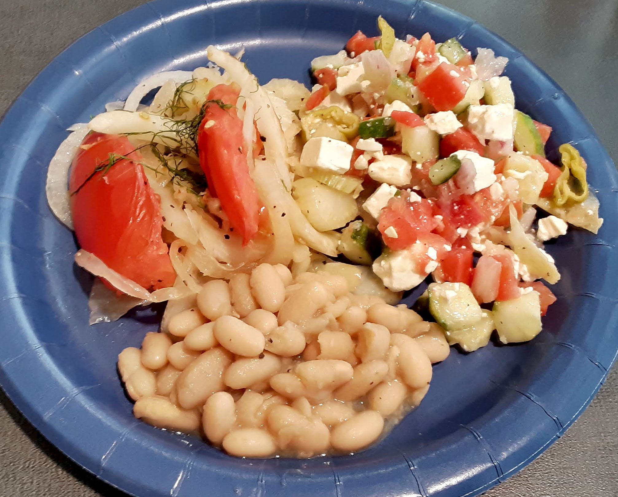On a paper plate, there is a scoop of canella beans, a Greek salad, and a pile of veggies. Photo by Paul Young.