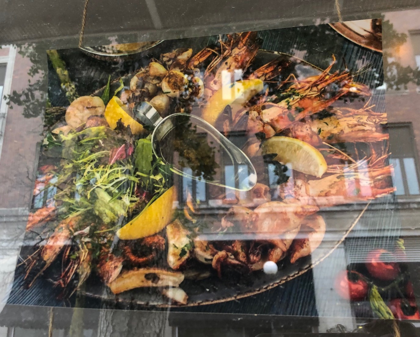 In a color print out of a photo taped to the inside of a window, there is a black bowl of seafood and shellfish with lemon wedges and herbs. Photo by Alyssa Buckley.