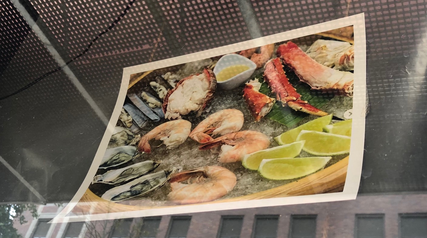 In a color print out taped to the inside of a window, there are many kind of shellfish in a bowl prepared fresh. Photo by Alyssa Buckley.