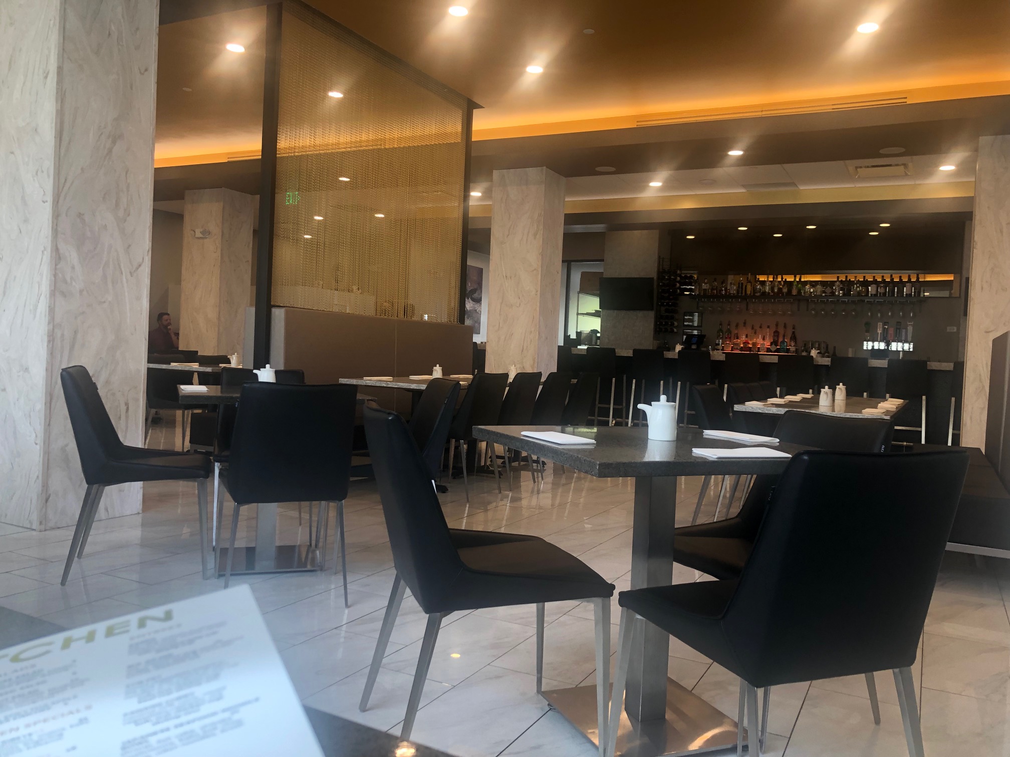 In the dining room, there are several empty tables with black chairs on a marble floor in the new KoFusion location in Downtown Champaign. Photo by Alyssa Buckley.