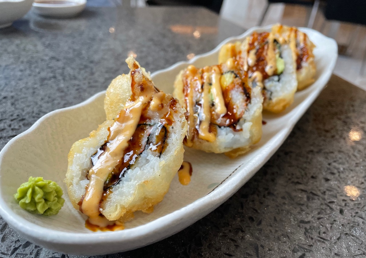 On a white tray, there is a fried sushi roll drizzled with two sauces. Photo by Alyssa Buckley.