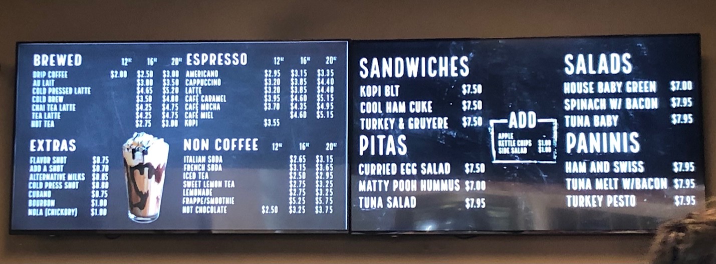 A long and skinny (and slightly blurry) photo of the Cafe Kopi television menu boards at the campus location. Photo by Alyssa Buckley.