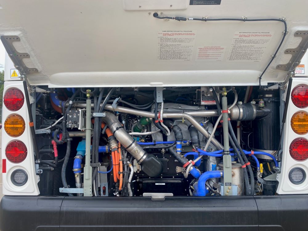 A close up of the inner workings of a hydrogen fuel cell bus. There are various tubes and pipes twisted around each other, and they are all very clean. Photo by Julie McClure.