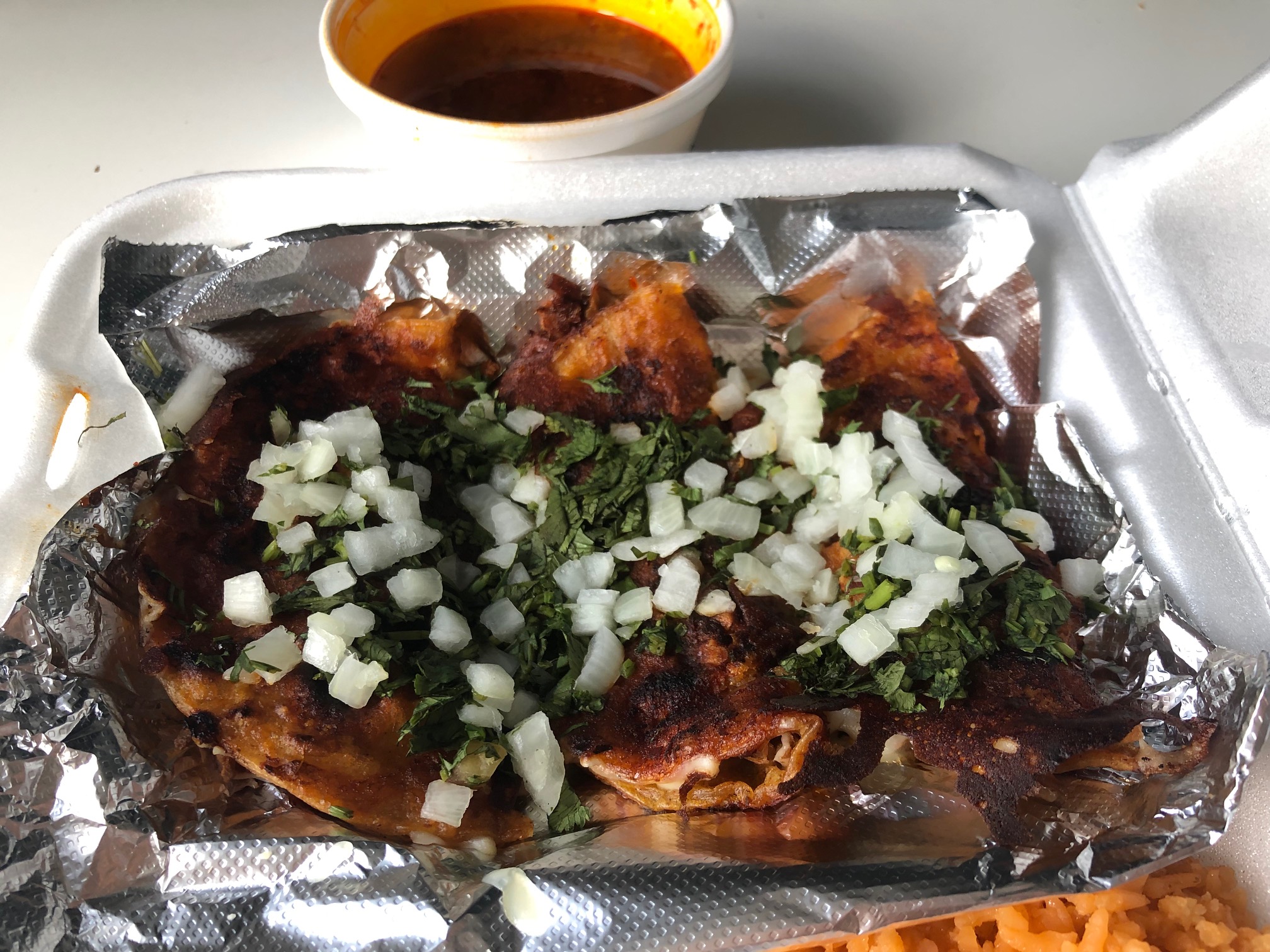 In a white styrofoam container, there are three birria tacos on tin foil. Photo by Alyssa Buckley.