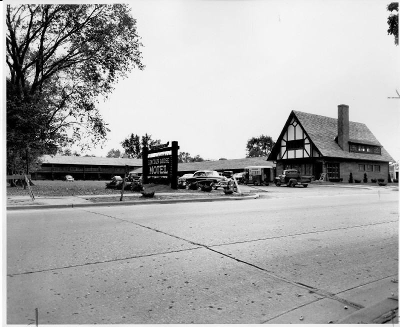 Black and white photo of a single story motel. On one end is a steep gable roof. A sign out front reads Lincoln Lodge Motel, and 1950s style cars are parked in the lot. Photo from University of Illinos Archives. 
