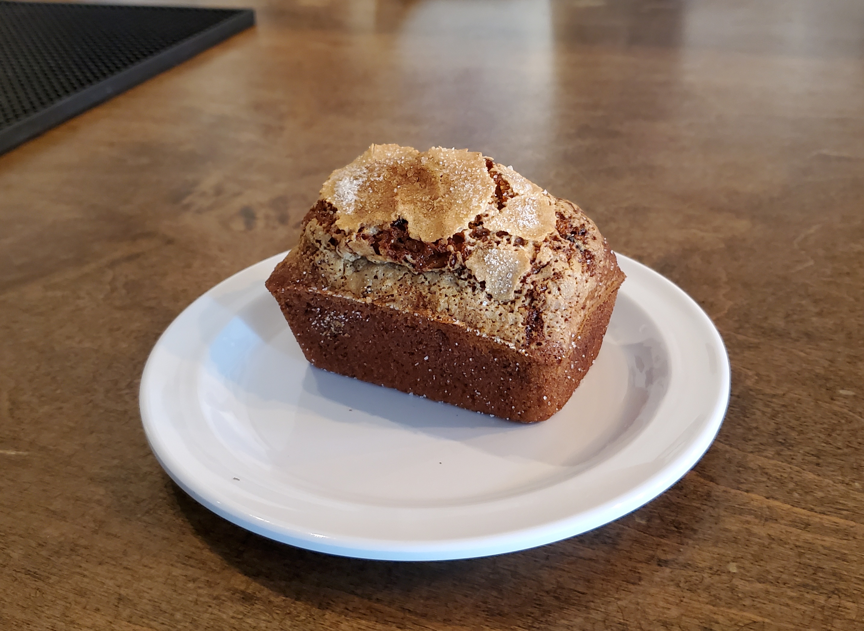 On a brown table, there is a mini loaf of zucchini bread on a small white circular plate. Photo by Rafay Khan.