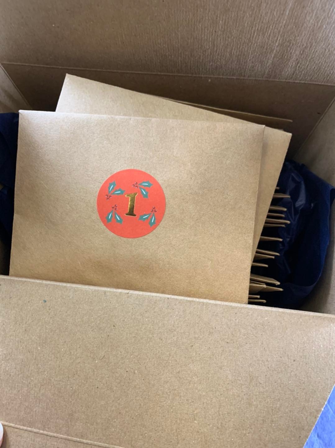 In a paper box, there are brown numbered envelopes with circle stickers with a number. The top envelope has a sticker with the number 1 on it. Photo from Walnut Street Tea Company's Facebook page.