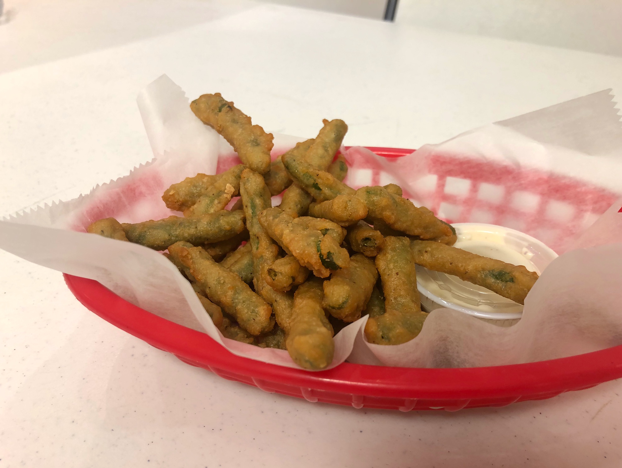 In a red plastic basket, there is a serving of fried green beans on parchment paper. Photo by Alyssa Buckley.
