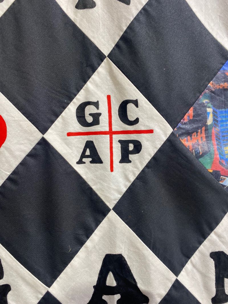 A close up of a quilt panel with a black and white Harlequin style pattern. In the center are intersecting red lines with GCAP in black block letters in each quadrant. Photo by Julie McClure with permission from Spurlock Museum.