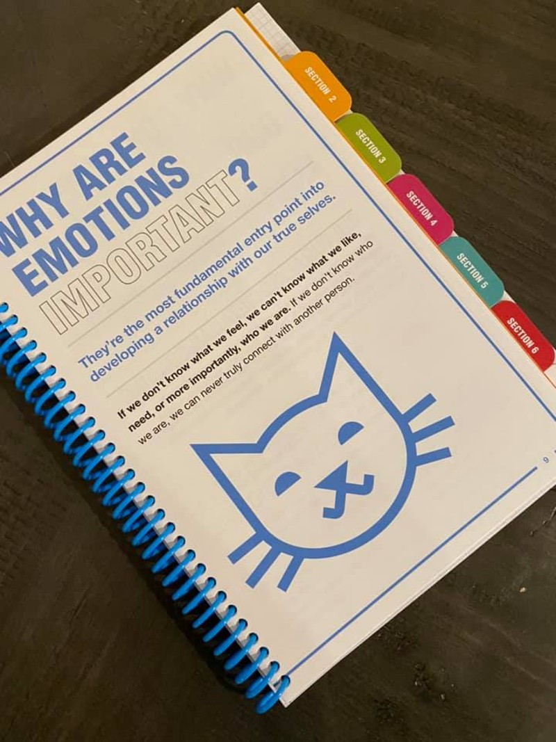 A spiral bound book with multi-colored tabs along the side. It's open to a page with a drawing of a cat face, and a heading that says Why are Emotions so Important? in block letters. Photo from Blueprint Facebook page.