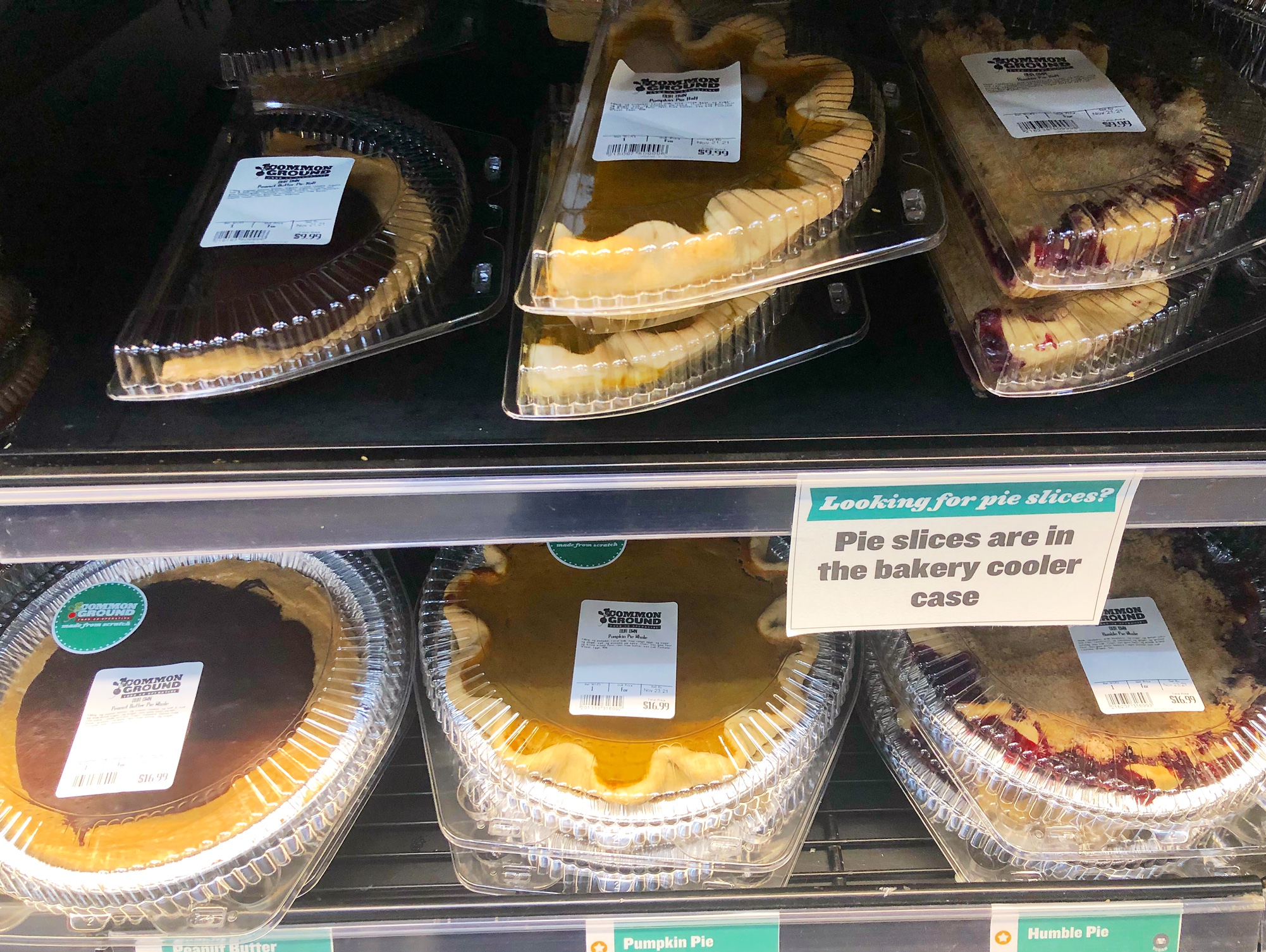 On the shelves at Common Ground, there are half pies in a tin with a plastic cover and full pies in a tin with a plastic cover. The transparent covers reveal a variety of pie flavors. Photo by Alyssa Buckley.