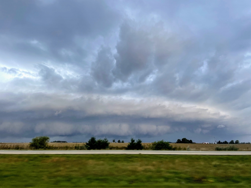 A low hanging shelf cloud extends across the horizon. The sky is dark and gray, with a field in the foreground. Photo by Andrew Pritchard. 