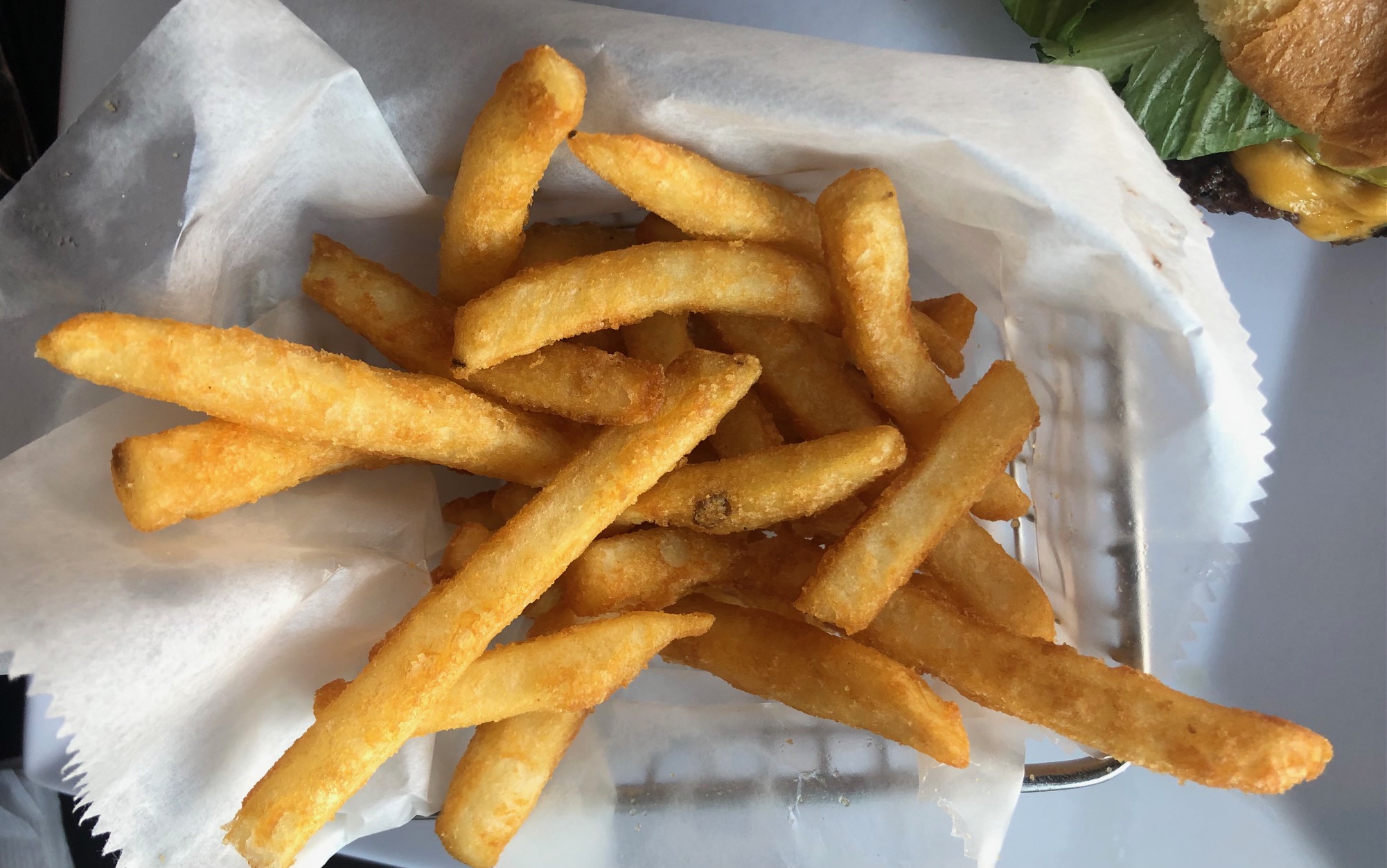An overhead photo shows freshly fried fries in a metal basket lined with parchment paper. Photo by Alyssa Buckley.