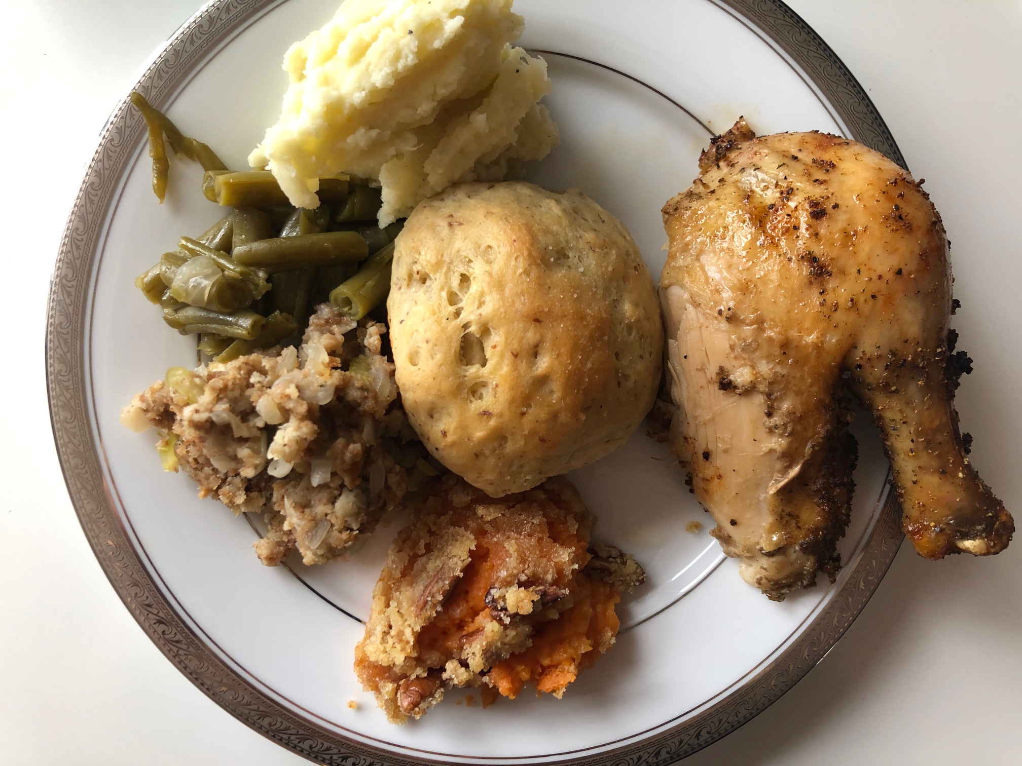 An overhead photo shows a plate of Thanksgiving food: a drumstick and thigh, a roll, stuffing, green beans, and mashed potatoes. Photo by Alyssa Buckley.