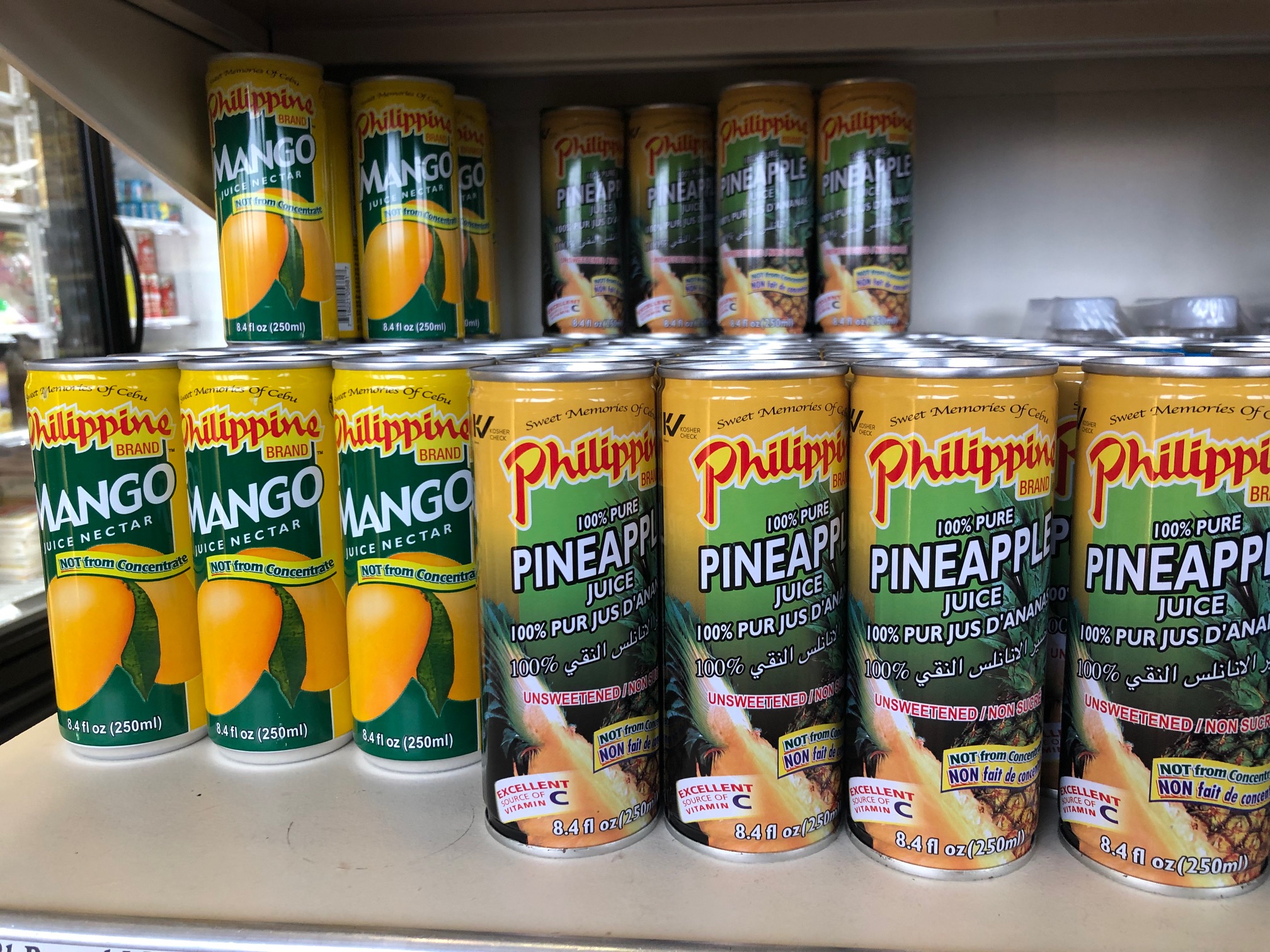 On a shelf, several cans of mango and pineapple juice are labels-forward on a shelf. Photo by Alyssa Buckley.