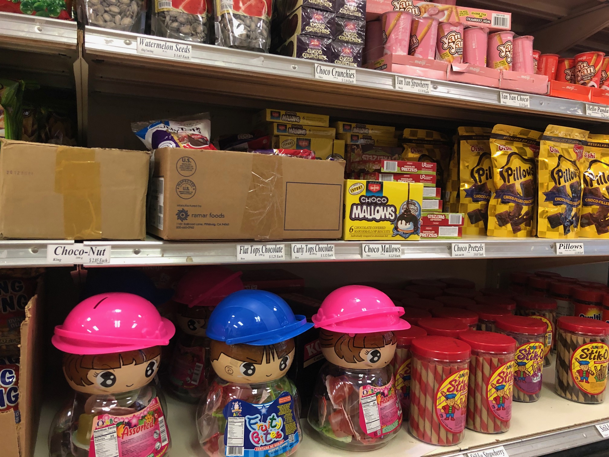 On the shelves, there are several chocolate sweet options. On the bottom shelf, there are three child-like containers with hard hats, and inside the transparent body, there are fruity candies. Photo by Alyssa Buckley.