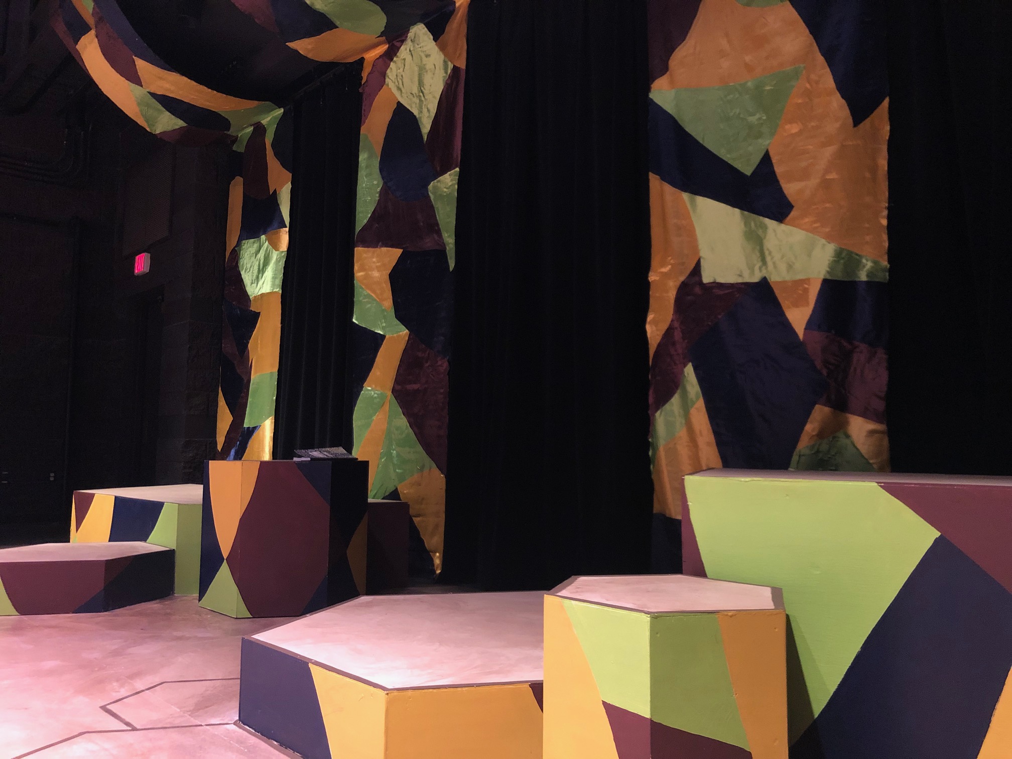 Onstage, there are a handful of hexagon outlines on the floor in addition to a collection of miniature stages of varied heights with a single black composition notebook atop one. Photo by Alyssa Buckley.