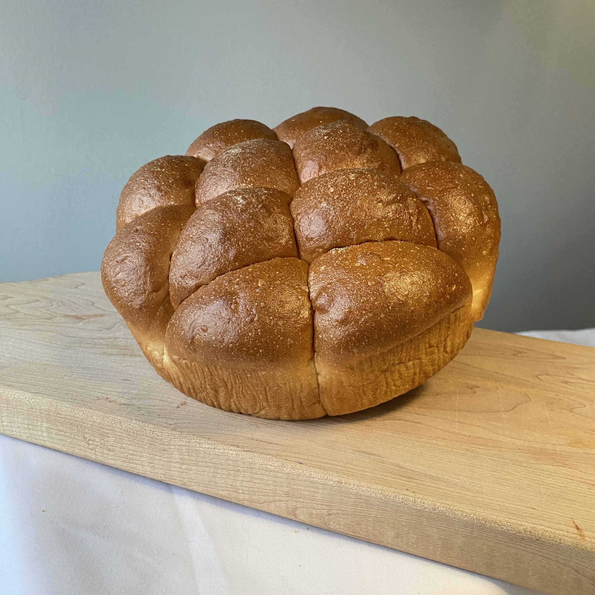 A large pull-apart bread roll sits on a wooden board on a white counter. Photo from Central Illinois Bakehouse website.