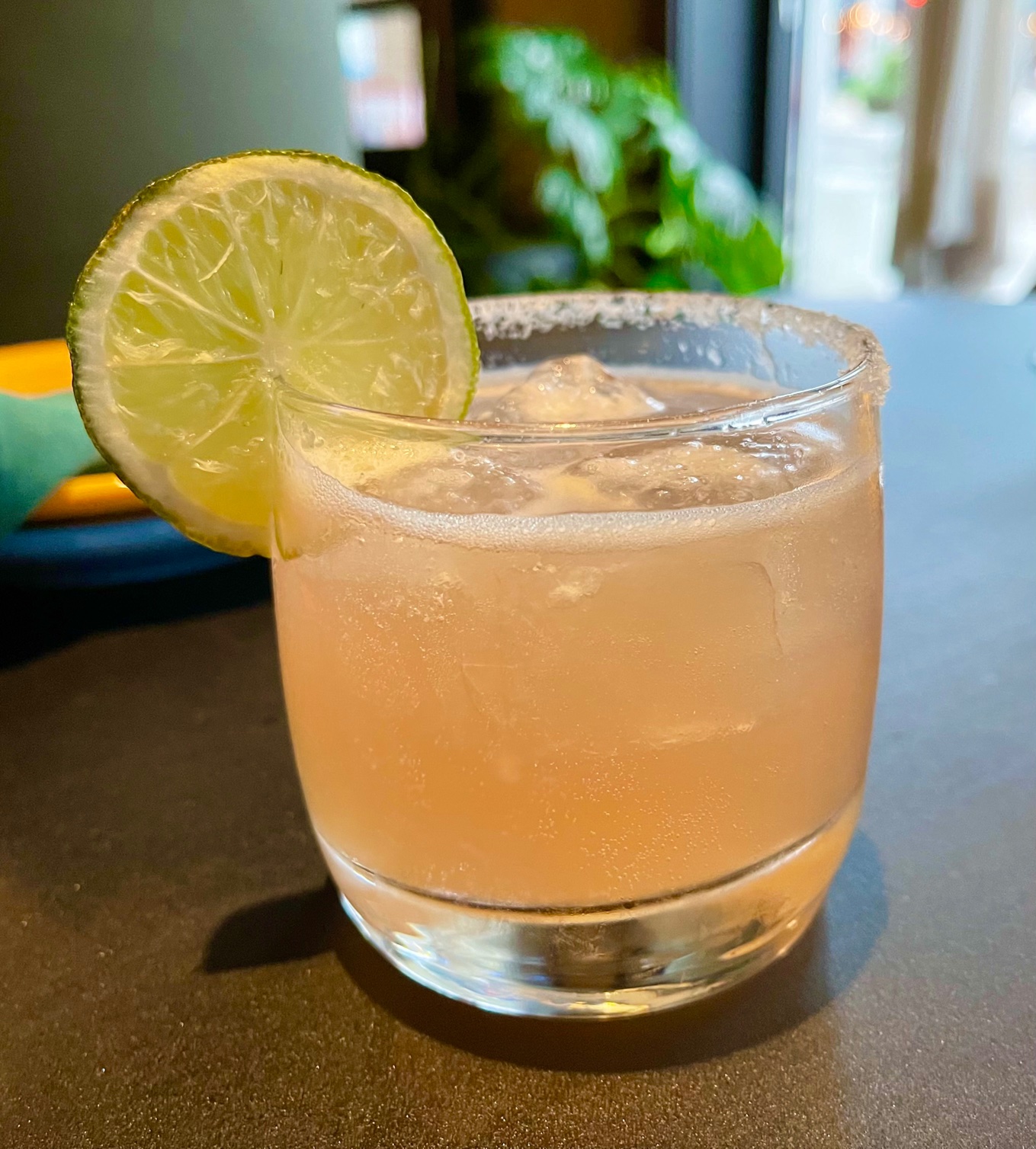 On a gray counter, there is a yellow drink in a half tumbler with a lime garnish. Photo by Stephanie Wheatley.