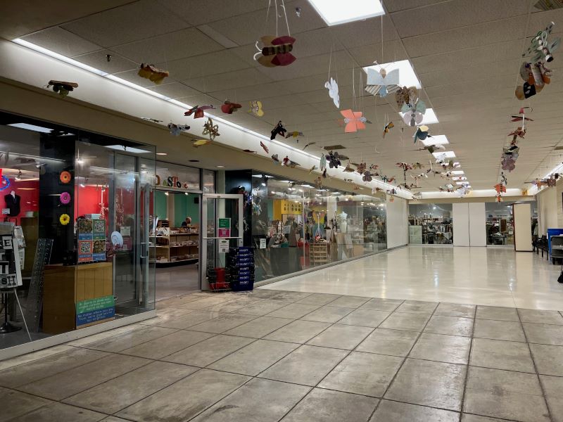 A large hallway with storefronts on either side, paper butterflies are hanging from the ceiling. Photo by Julie McClure.