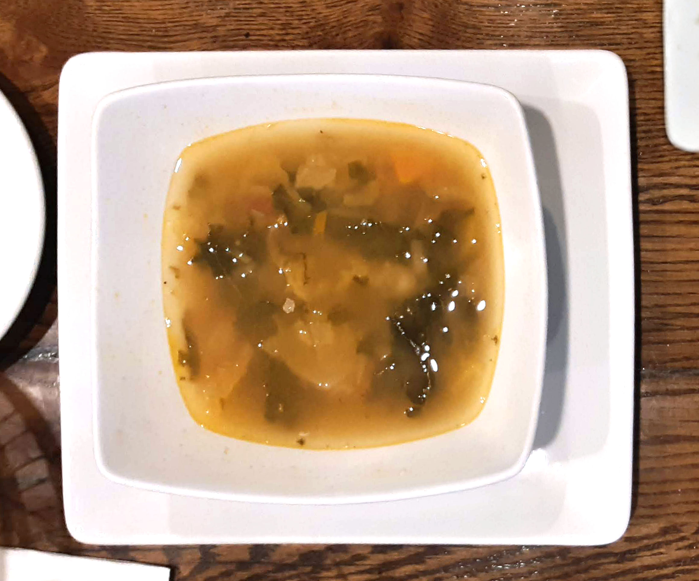 On a large square plate, there is a smaller square bowl with a dark brown cloudy minestrone soup. Photo by Paul Young.