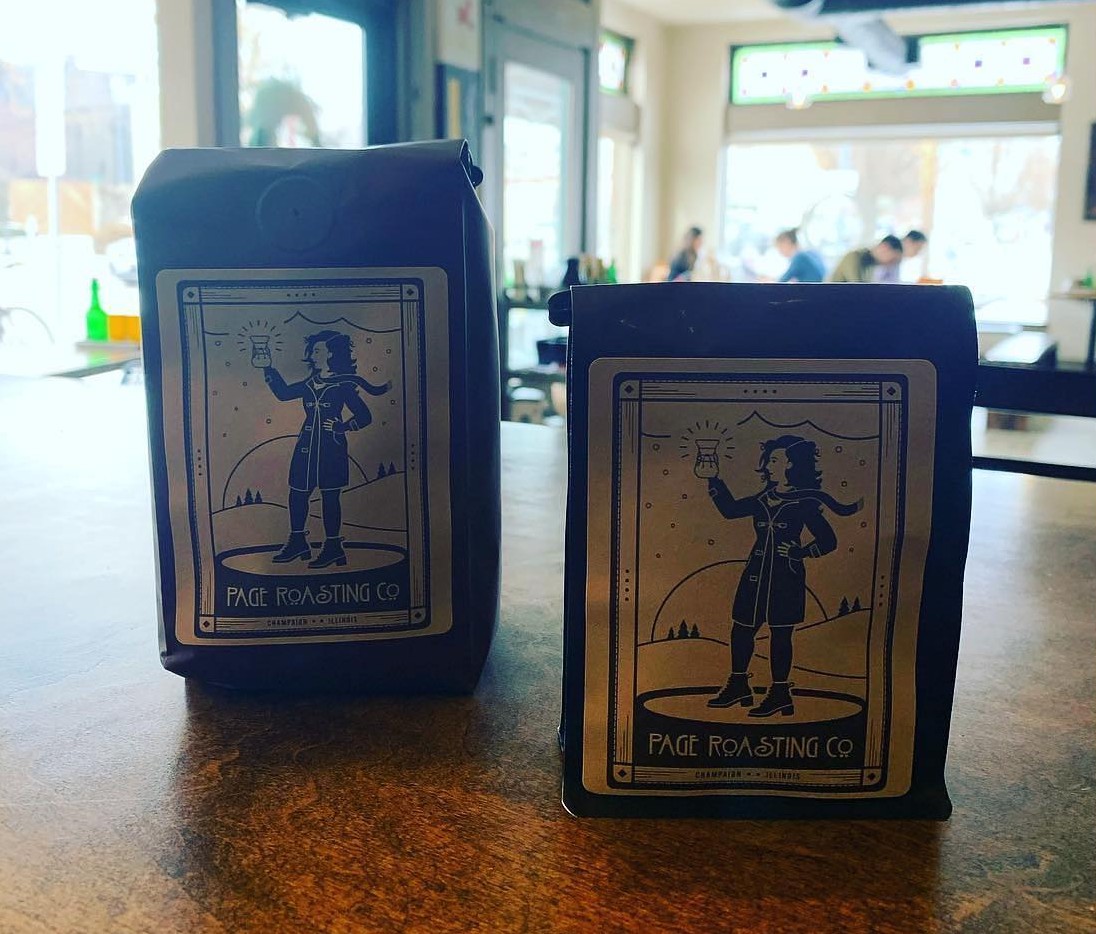 Two bags of coffee beans sitting on a countertop. The bags are copper colored, and the label has a black and white print of a women holding up a pourover coffee container. Photo from Page Roasting Company Facebook page.