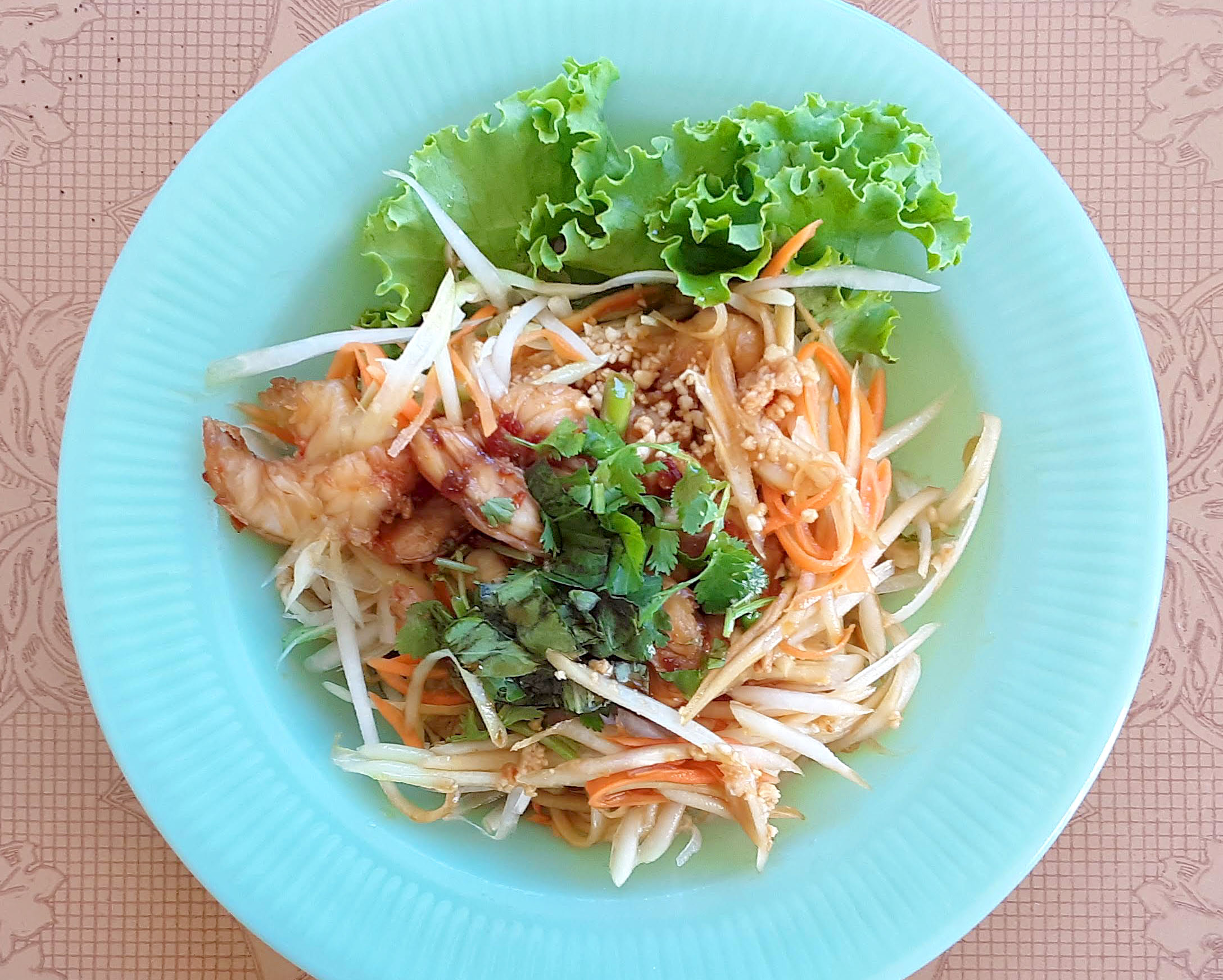 On a blue plate, there is a brightly colored fresh papaya salad. Photo by Paul Young.