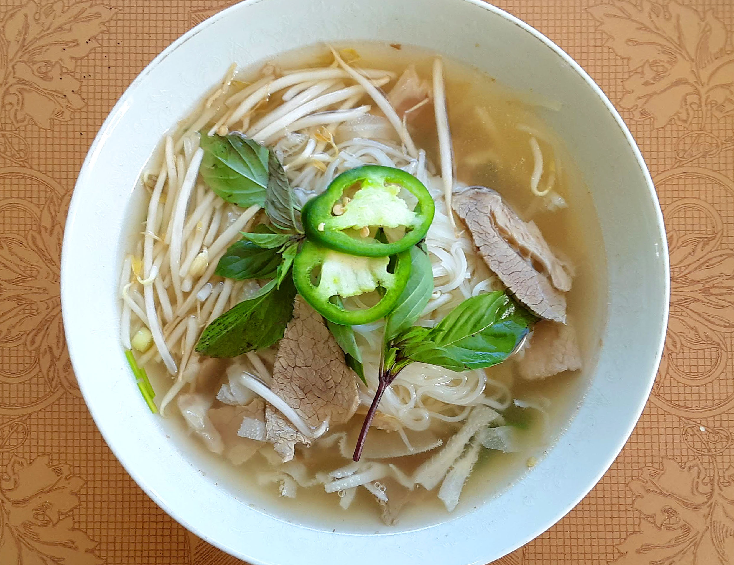 In a white bowl, there is pho with sliced jalapenos, white bean sprouts, and beef slices. Photo by Paul Young.