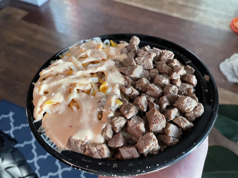 In a plastic black bowl, there is a burrito bowl. Half of the bowl is chopped steak bites, and the other is rice covered in a light orange sauce. Photo by Anthony Erlinger.