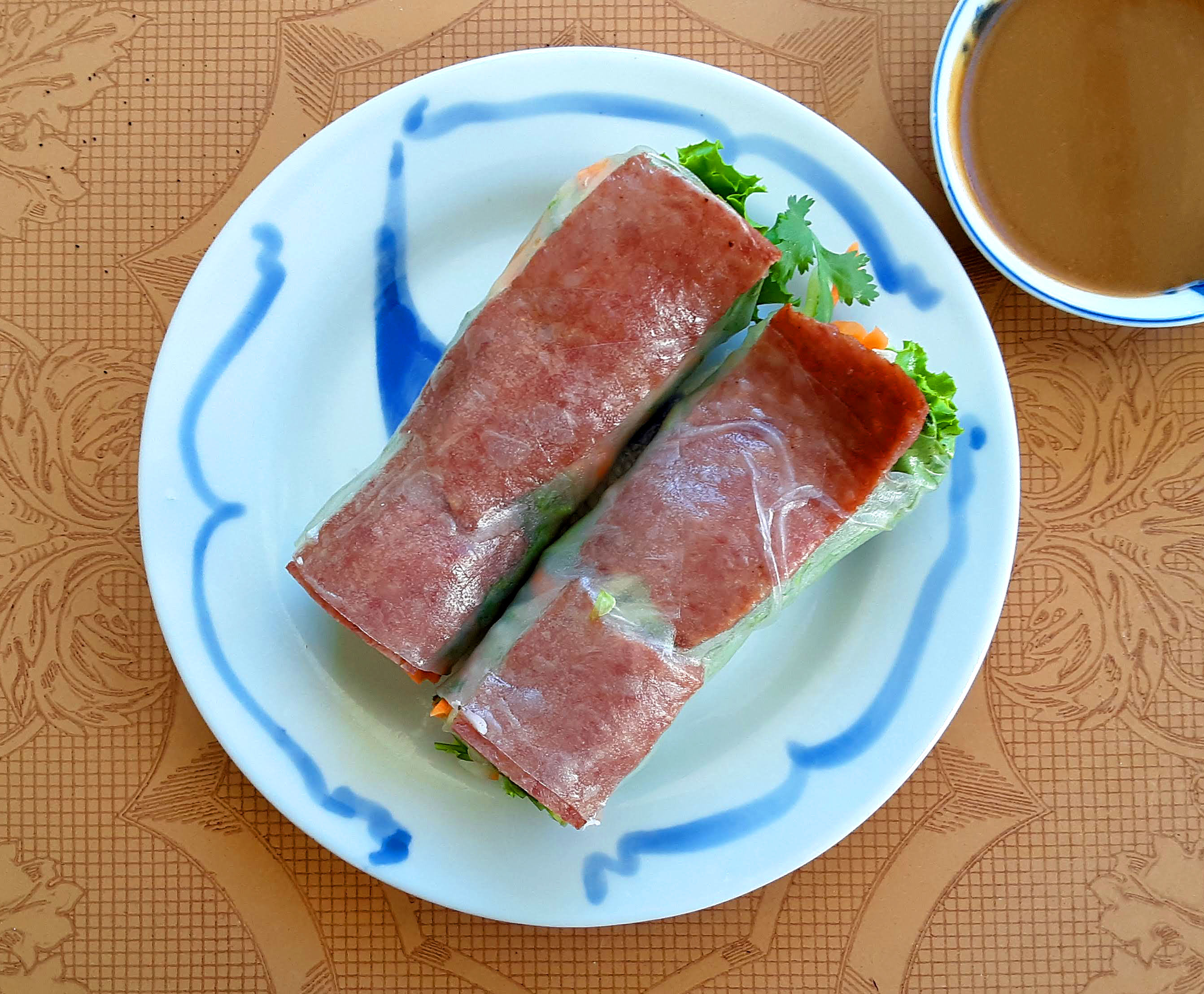 On a white plate with blue streaks on the border, there are two soft summer rolls from Xinh Xinh Cafe. Photo by Paul Young.