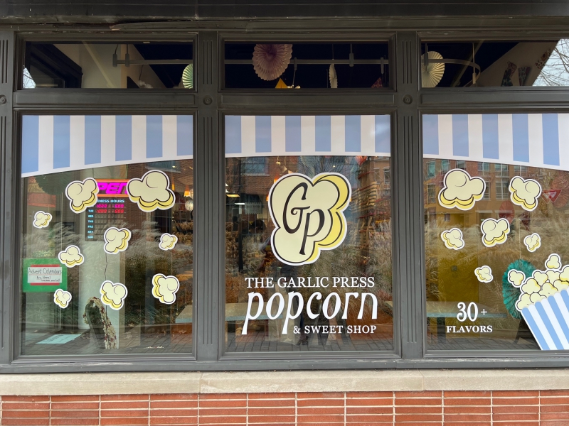 A store window with blue and white stripes painted across the top. There are popcorn decals decorating the window. Photo by Julie McClure.