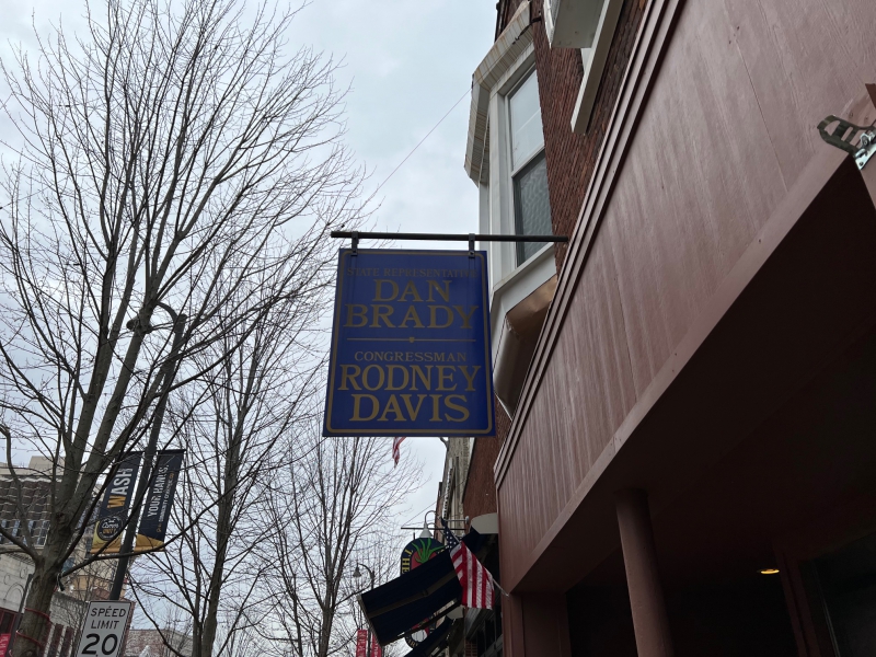 A blue sign that says Dan Brady and Rodney Davis in gold writing. It hangs off the side of a brown building. Photo by Julie McClure.