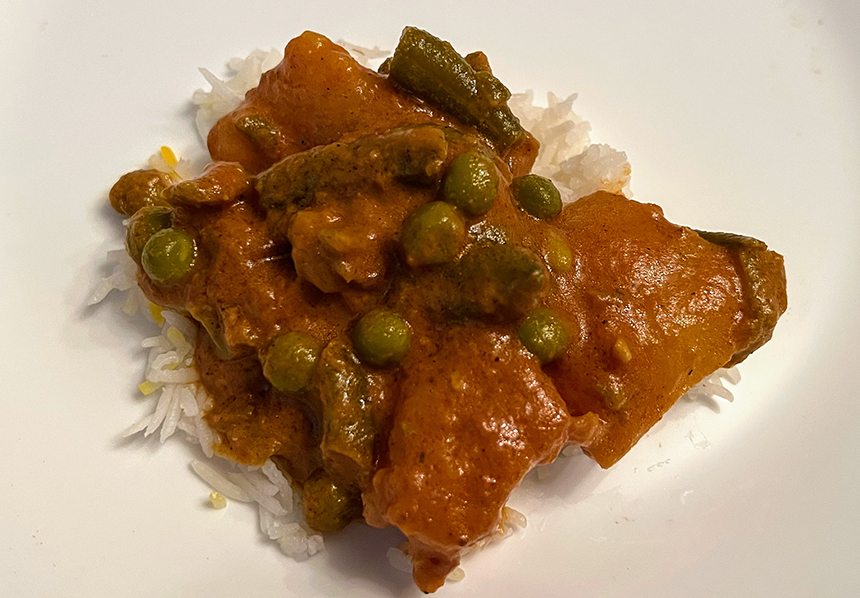 This is a close up photo of the dish: vegeterian korma on a small bed of rice. Large chunks of potato are speckled with green peas and green beans are coated in a creamy red sauce. IN the sauce you can see specks of spices.  Photo by Sara Ressing.