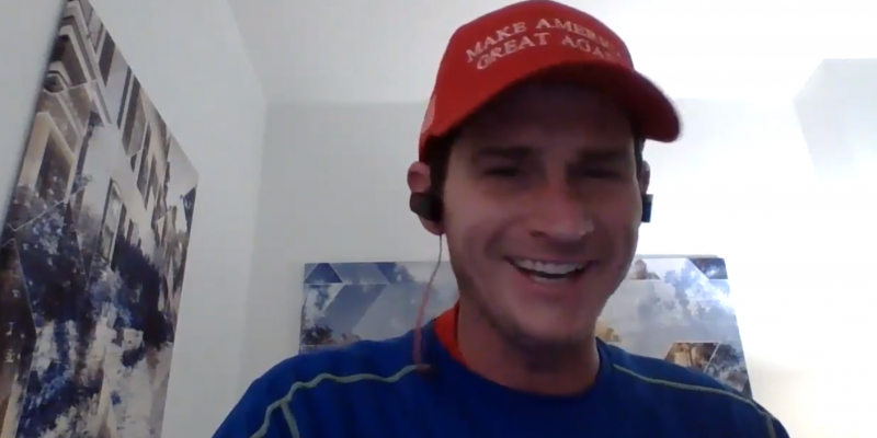 A moron in a mostly white room smiling, wearing headphones and a red MAKE AMERICA GREAT AGAIN hat.