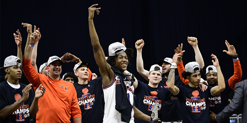 The Illini Basketball team with their hands in the air celebrating, wearing tournament championship hats