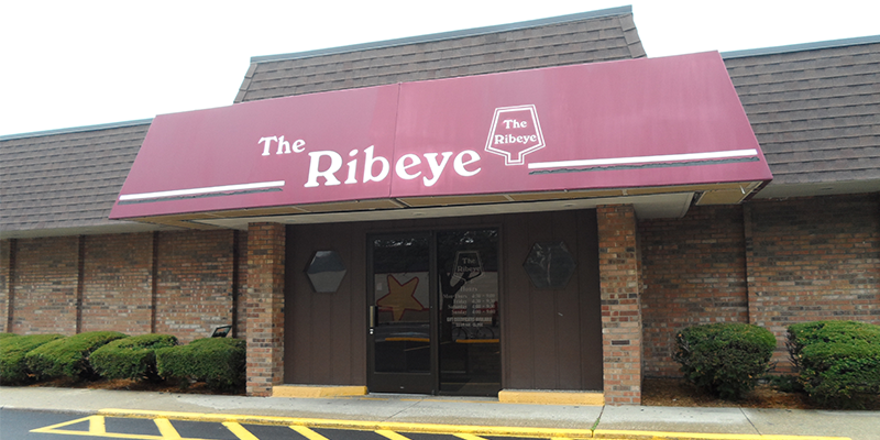 A brick building with a red awning for THE RIBEYE in white text.