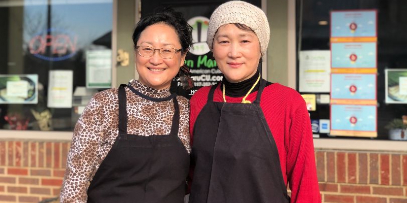 Two Korean women smiling at the camera in front of San Maru's storefront.